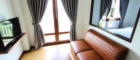 Una habitación con un sofá de cuero marrón, una mesa de centro de madera, un televisor de pantalla plana sobre un soporte de madera y un amplio ventanal con cortinas grises.