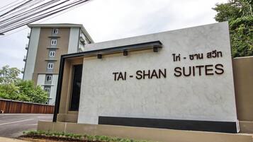Señal para Tai-Shan Suites, con un diseño moderno y vista a un edificio de varios pisos al fondo.