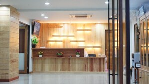 A reception desk with a wooden finish, a flat-screen TV, and a small plant. - Tai-Shan Suites (Ratchaburi)