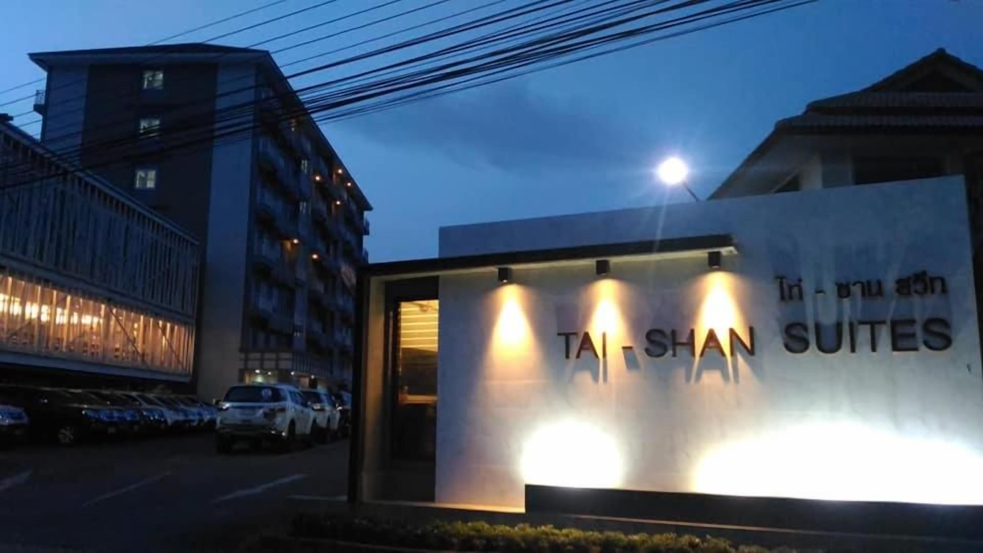 A building with a sign for 'Tai-Shan Suites' and a parking lot with cars.