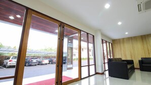A spacious lobby with large sliding glass doors leading to a parking area, a red carpet, and two black sofas. - Tai-Shan Suites (Ratchaburi)