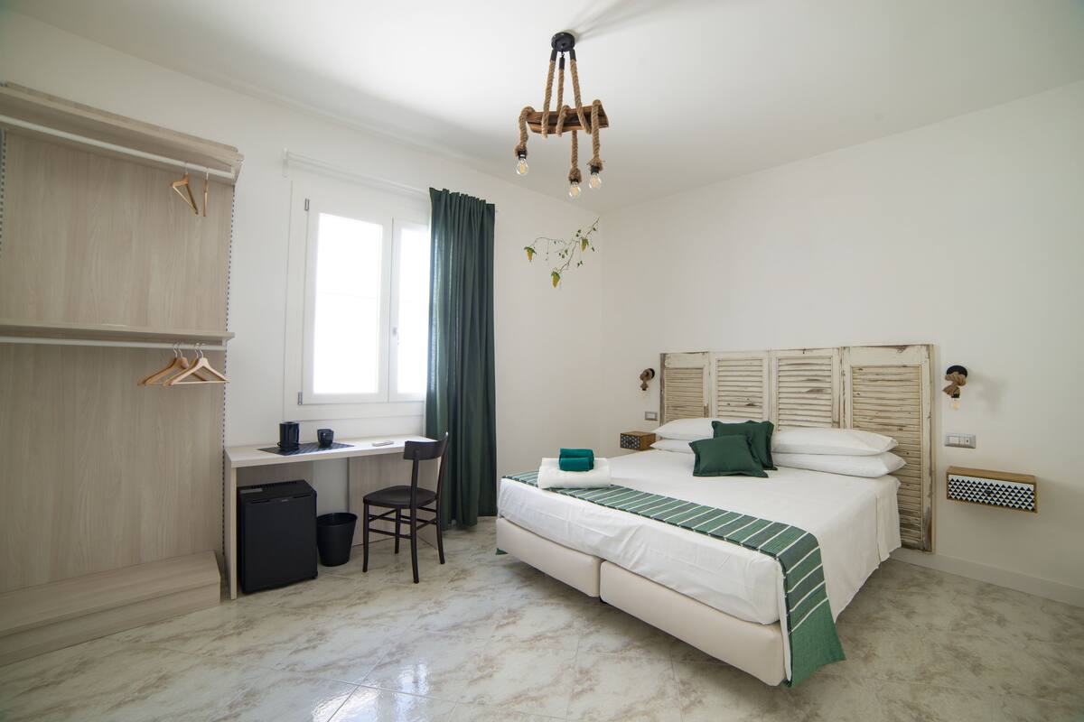 A bedroom with a bed, desk, chair, and a small trash bin.
