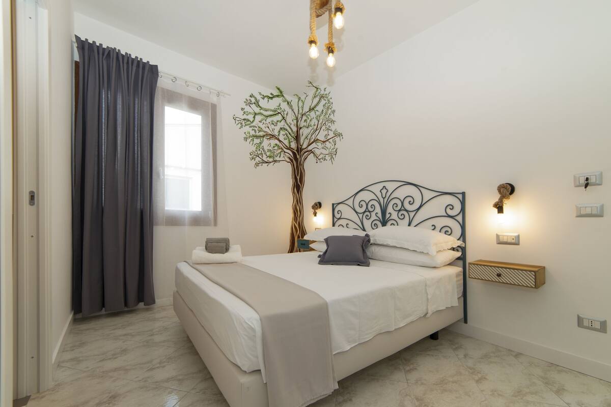 A bedroom with a bed, a wall-mounted tree decoration, and a nightstand with a lamp.