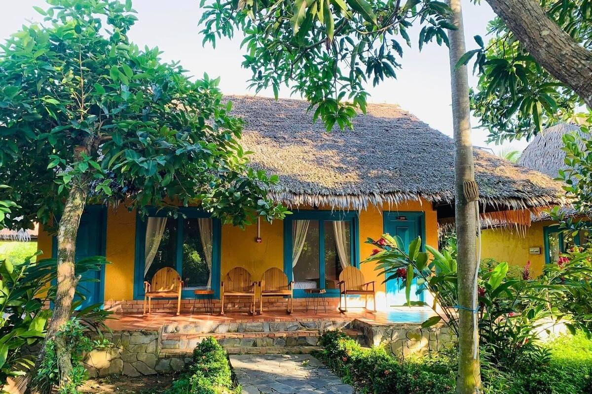 Een rieten bungalow met een pad van stenen dat naar de ingang leidt, omgeven door weelderige begroeiing.