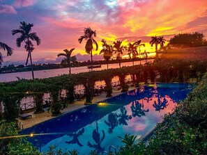 Ein Schwimmbecken mit Sonnenuntergangsblick, umgeben von Palmen und einem Wasserspiegel.