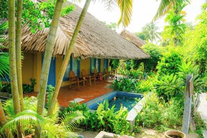 Ein Haus mit einem Strohdach und einem Pool, umgeben von üppigem Grün.