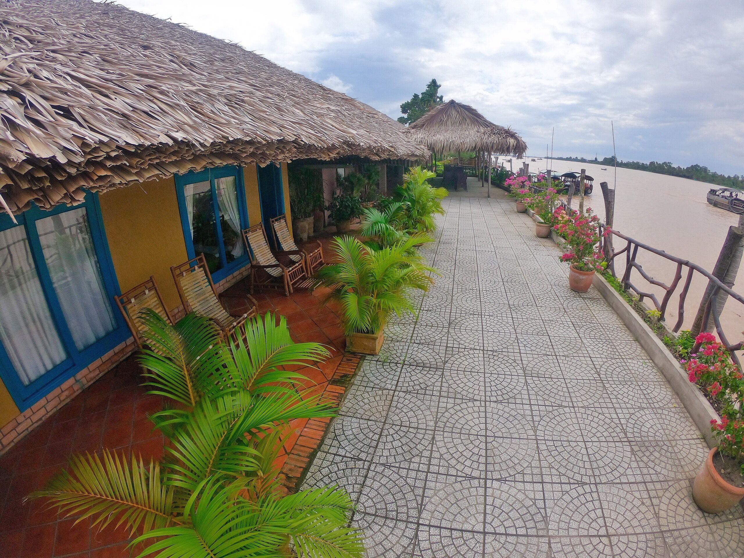 A terrace with thatched-roof huts, potted plants, and a tiled walkway.