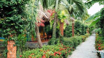 Un sendero en un jardín con muro de ladrillo, palmeras y flores rojas.