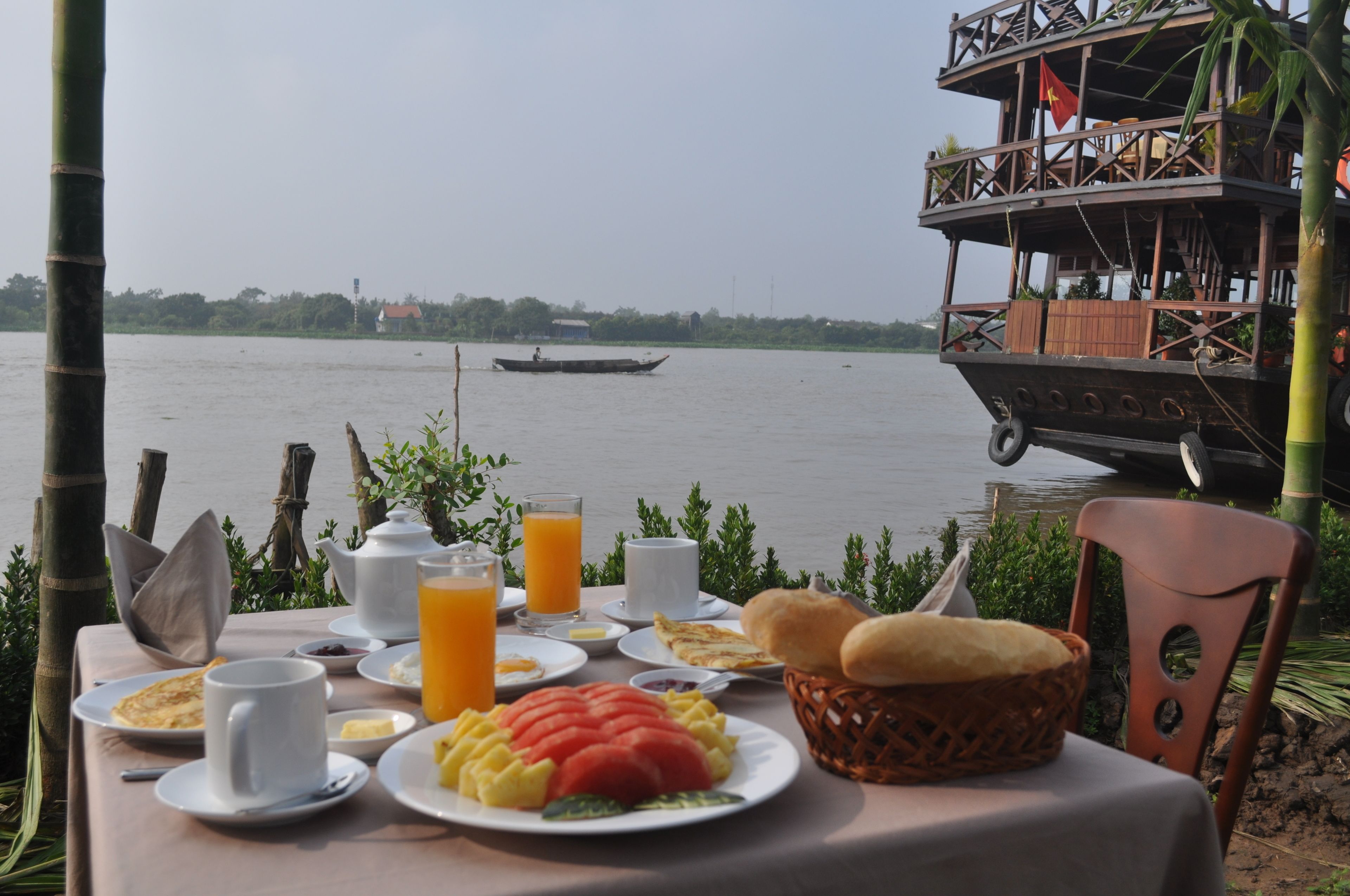Una tavola imbandita per la colazione, con vista su un fiume tranquillo e una barca in lontananza.