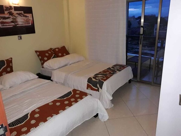A hotel room with two beds, a balcony with a view, and a painting on the wall.