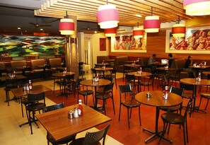 A restaurant with multiple tables and chairs, wooden ceiling with slats, and hanging pendant lights.