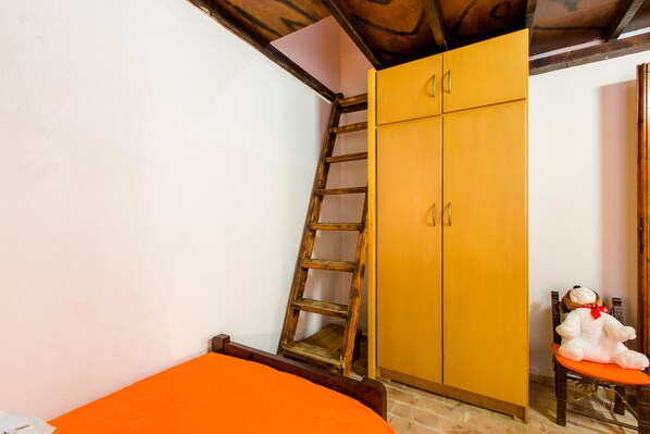 Una habitación con una cama, una escalera de madera, un armario y una silla con un peluche.