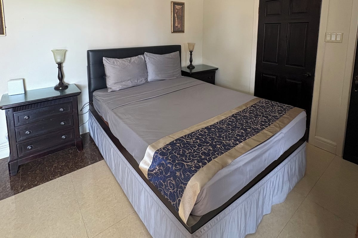 A bedroom with a bed, a nightstand, a ceiling fan, a door, and a framed picture on the wall.