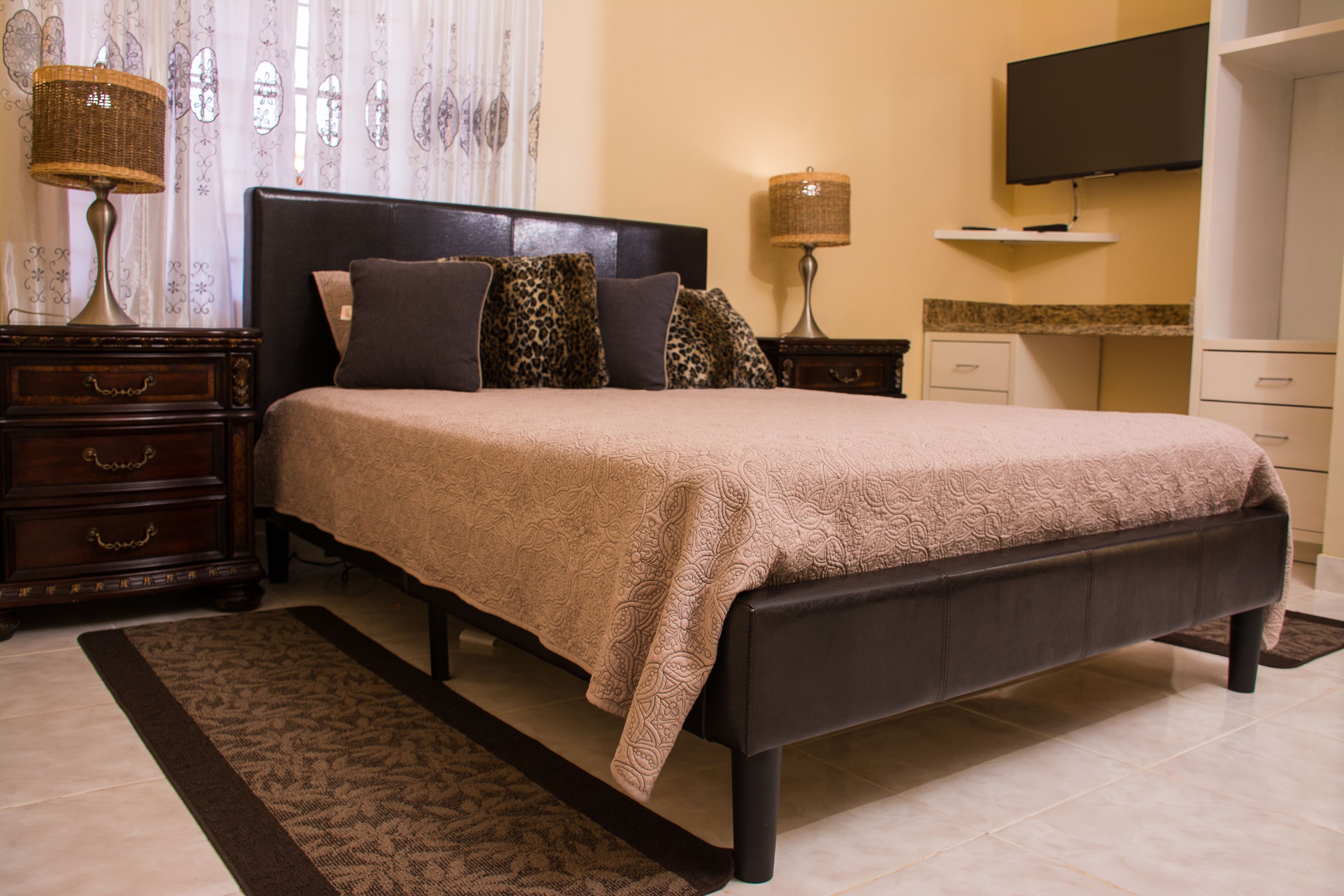 A bedroom with a large bed, two bedside tables, a television on the wall, and a small desk.
