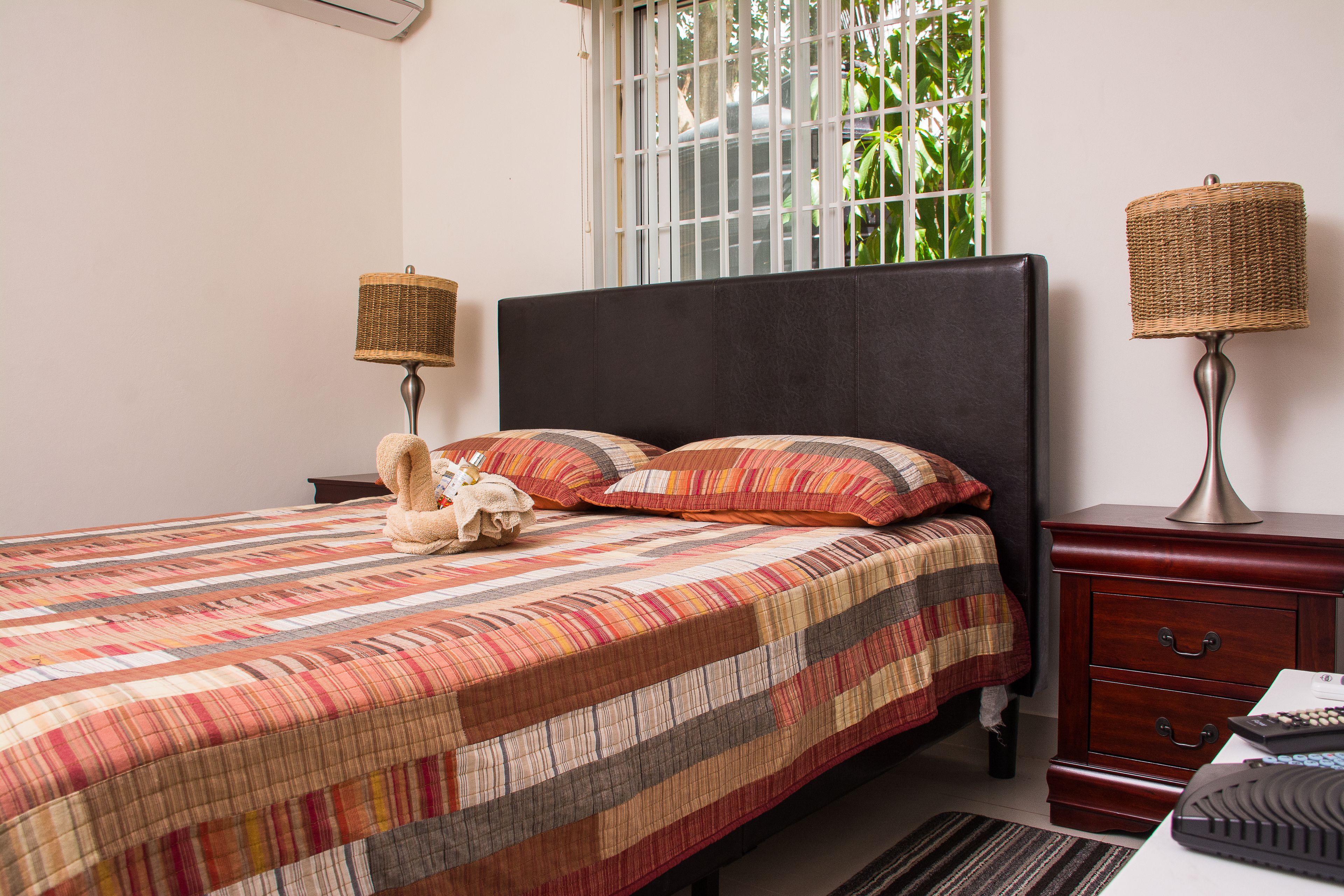 A neatly made bed with striped bedding, two bedside tables with lamps, and a window with a view of greenery.