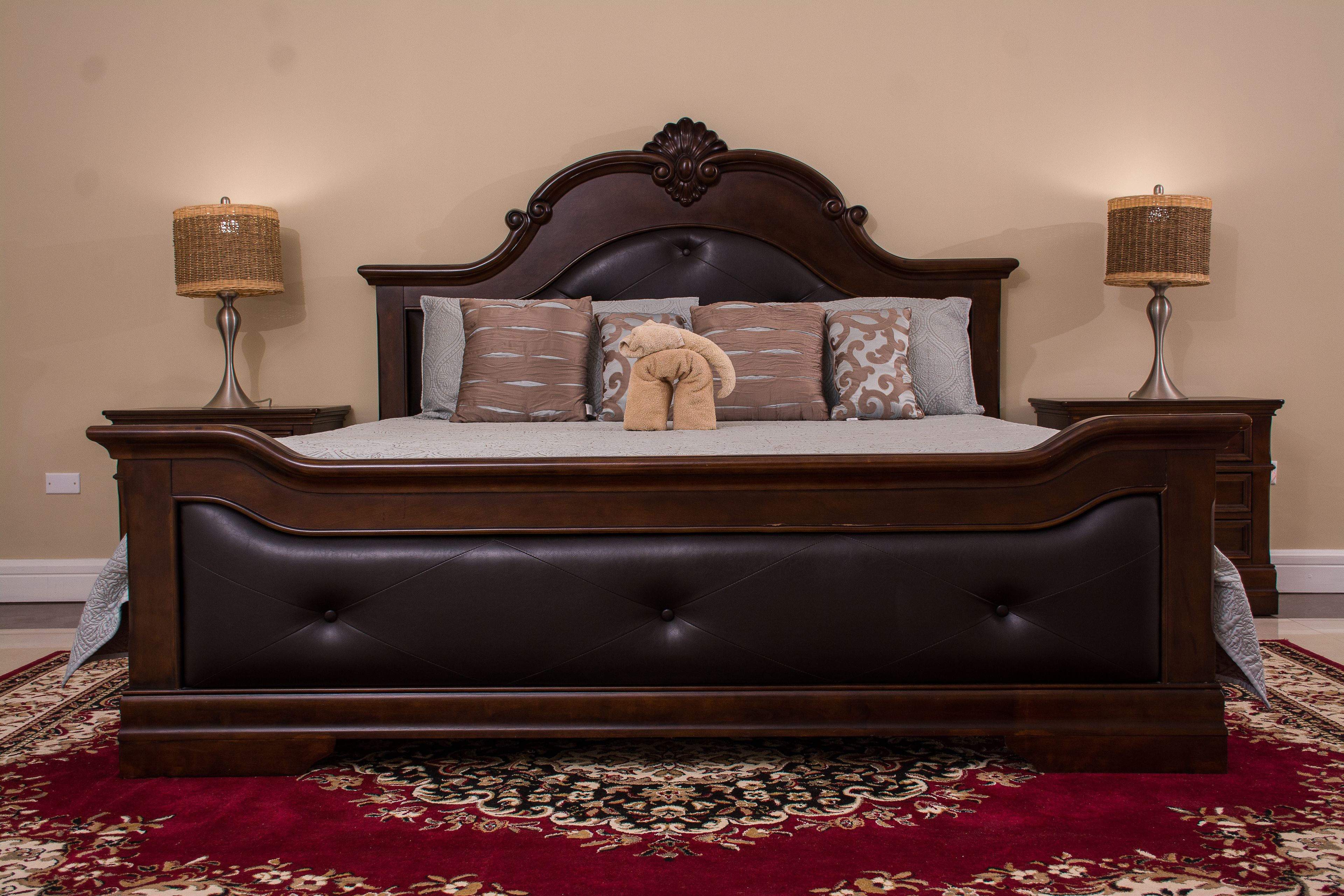 Una cama grande de madera oscura con un cabecero capitonado, dos lámparas de noche y un peluche de oso en las almohadas.
