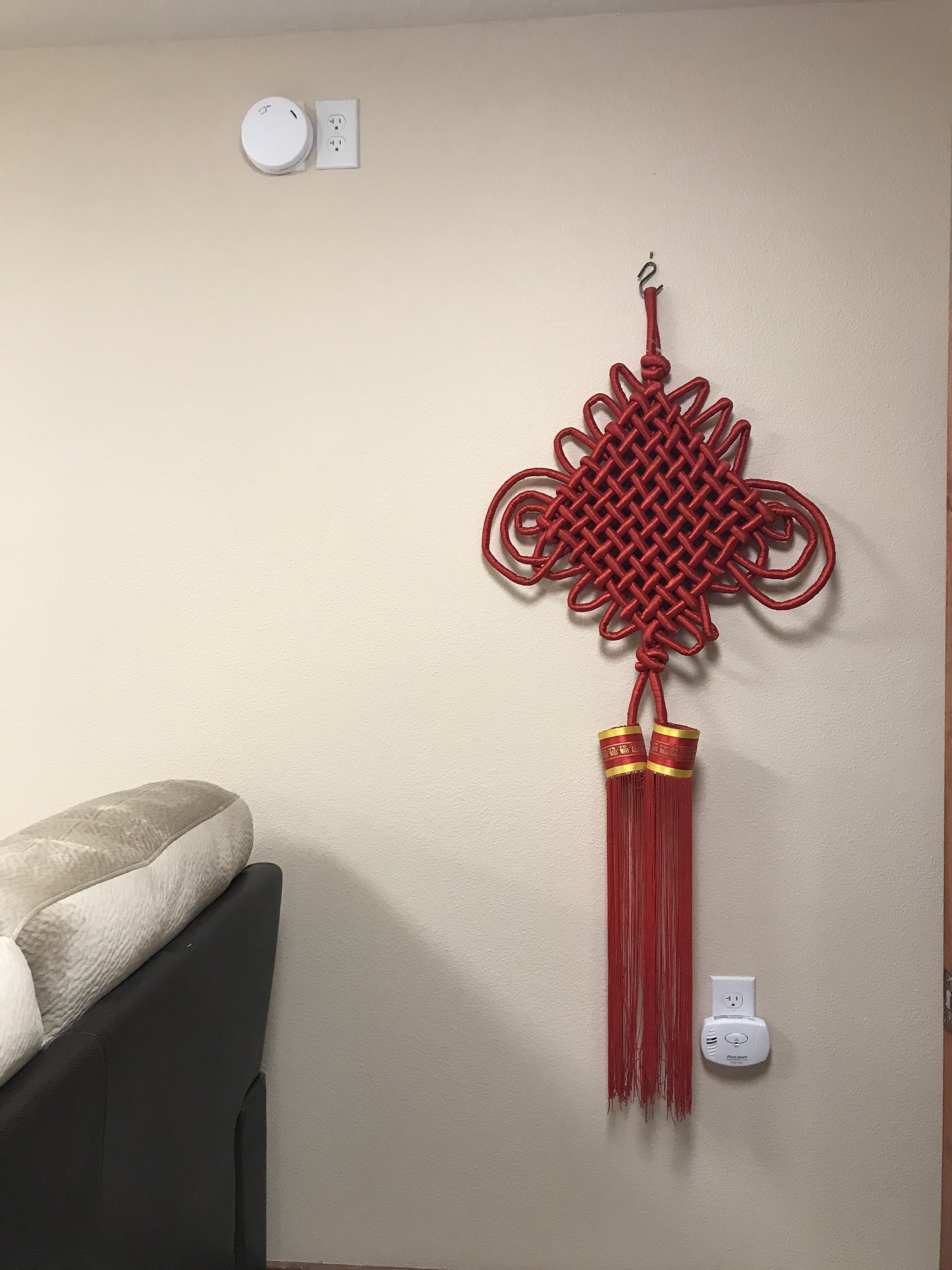 A wall-mounted red decorative piece with a tassel, a power outlet, and a thermostat.