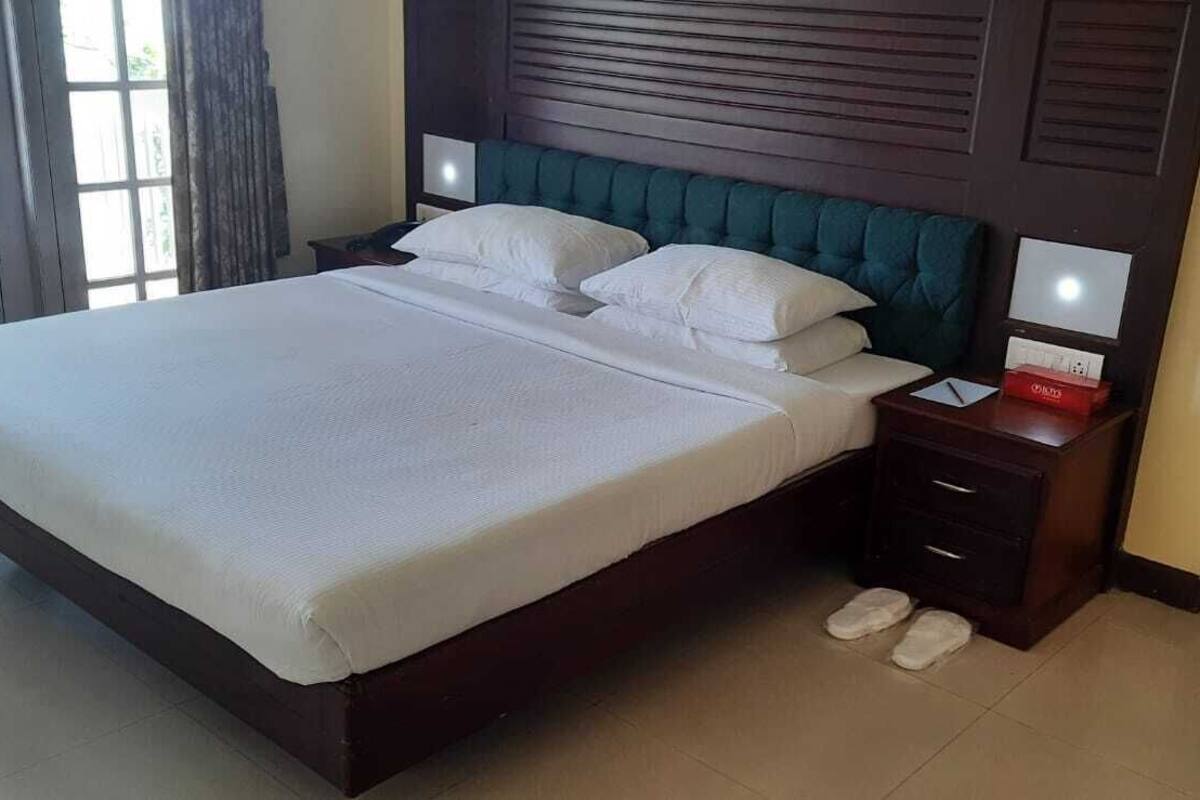 A neatly made bed with white linens, a dark wooden headboard, and a bedside table with a lamp and a red box.