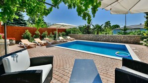 Un patio trasero con piscina, sillas de descanso y una mesa.