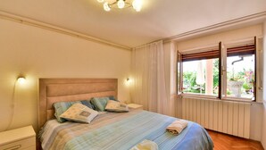 Un dormitorio con cama, mesitas de noche, una ventana con cortinas y una lámpara de techo.