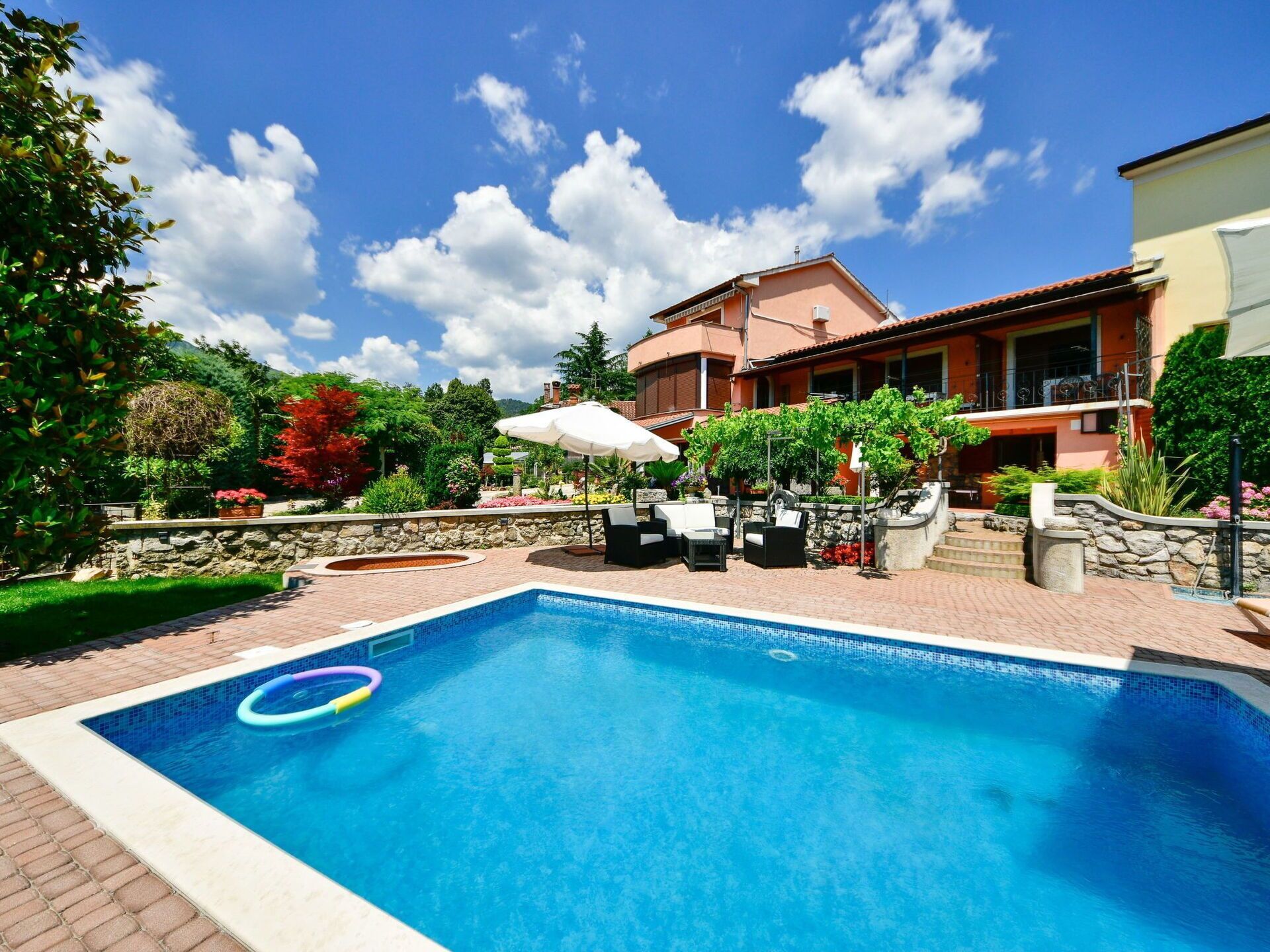 Ein Pool mit Liegestühlen und Sonnenschirmen, umgeben von einem Garten und einem Haus.