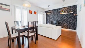 Un salon moderne avec un canapé blanc, une table à manger avec des chaises et un téléviseur fixé sur un mur à motifs.
