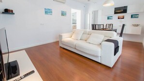 Un salon moderne avec un canapé blanc, un parquet et un téléviseur à écran plat.