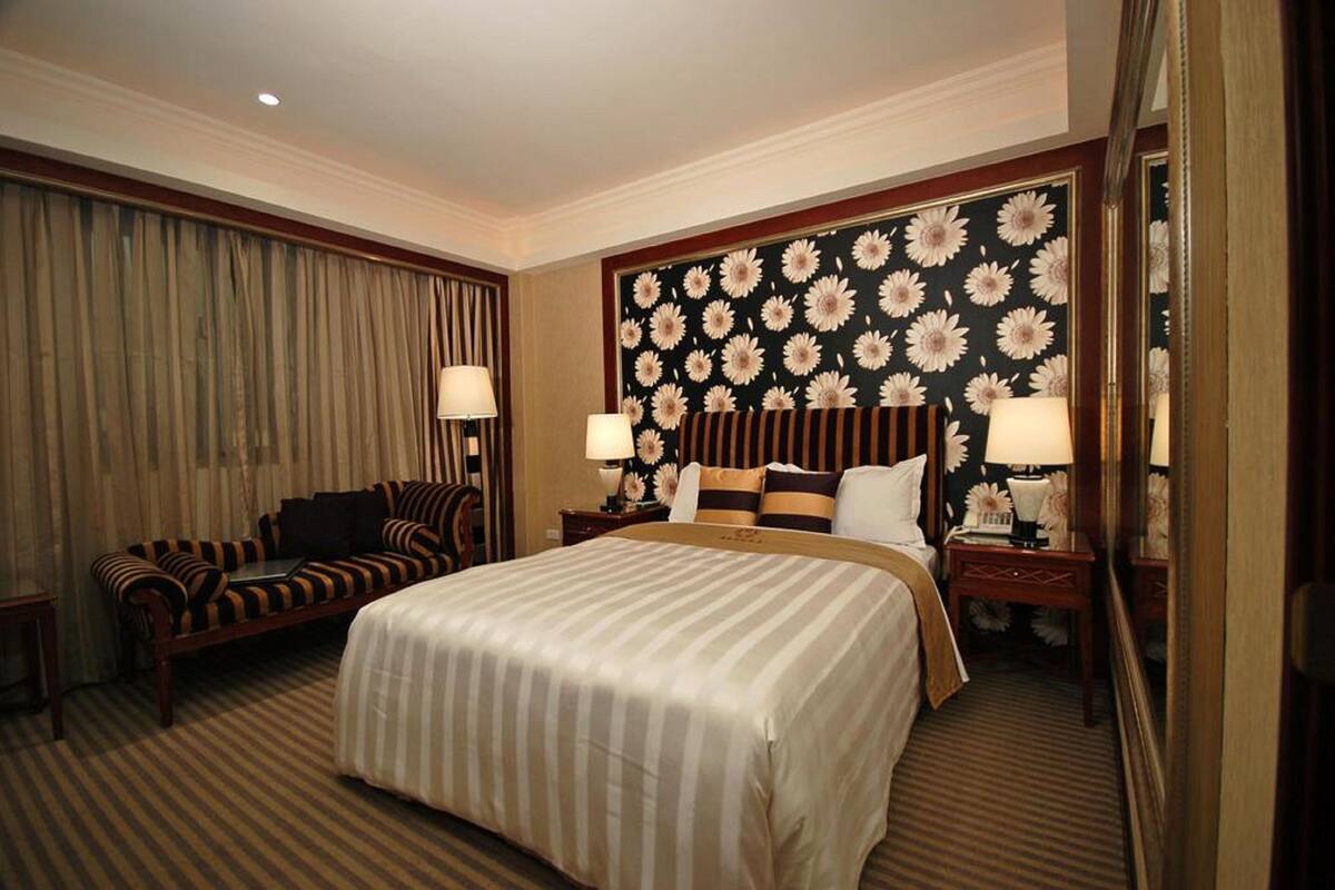 A hotel room with a large bed, a sofa, a nightstand, and a mirror.