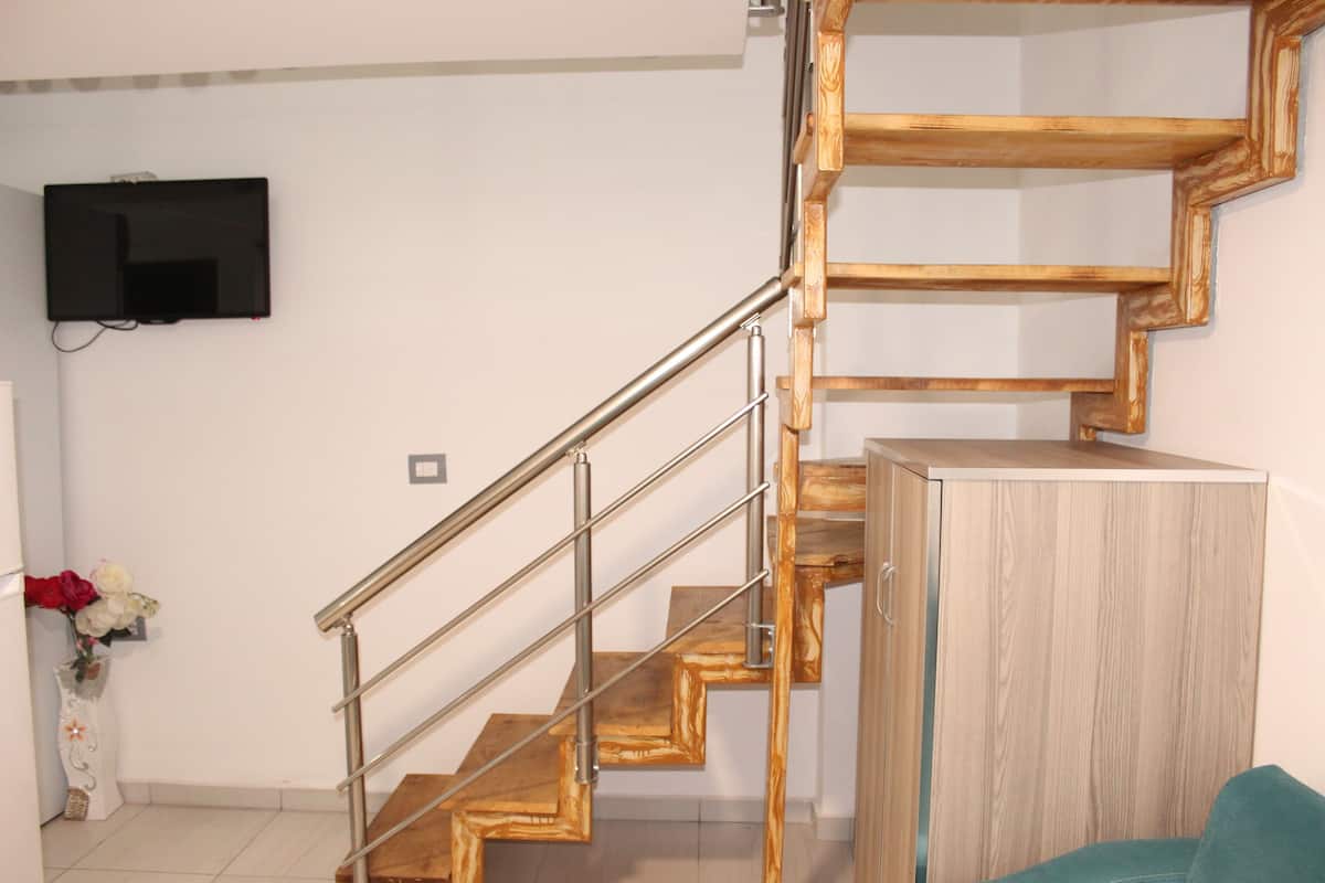 A staircase with wooden steps and metal railings, a flat-screen TV mounted on the wall, and a wooden cabinet.