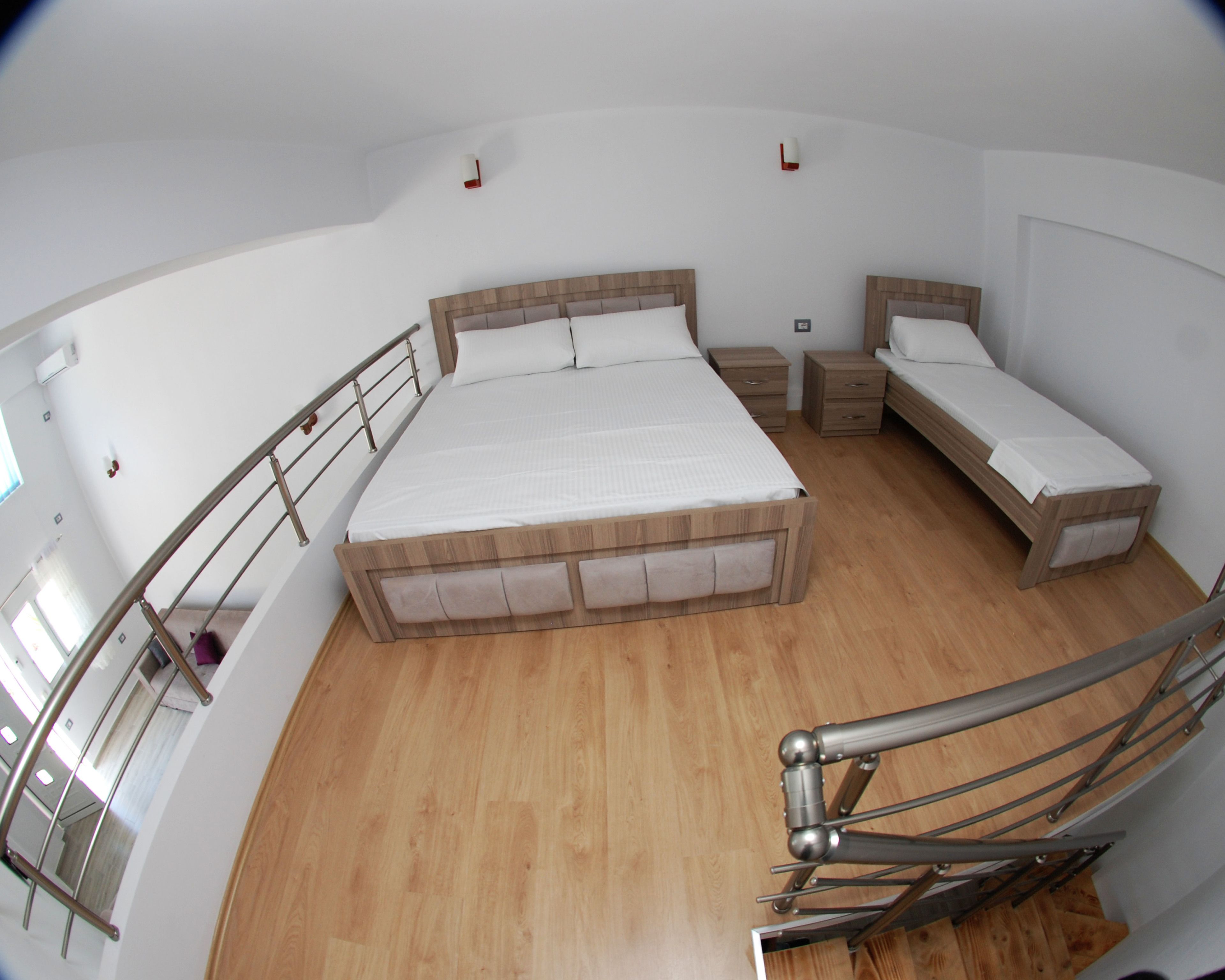 Un dormitorio con una cama grande, dos mesitas de noche, una cama más pequeña y una escalera.
