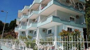 A multi-story building with balconies, air conditioning units, and a white fence in front. - Bebi Apartments (Sarandë)