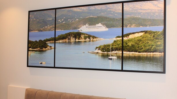 A bedroom with a bed, white pillows, a headboard, a wall-mounted air conditioner, and a framed landscape painting. - Bebi Apartments (Sarandë)