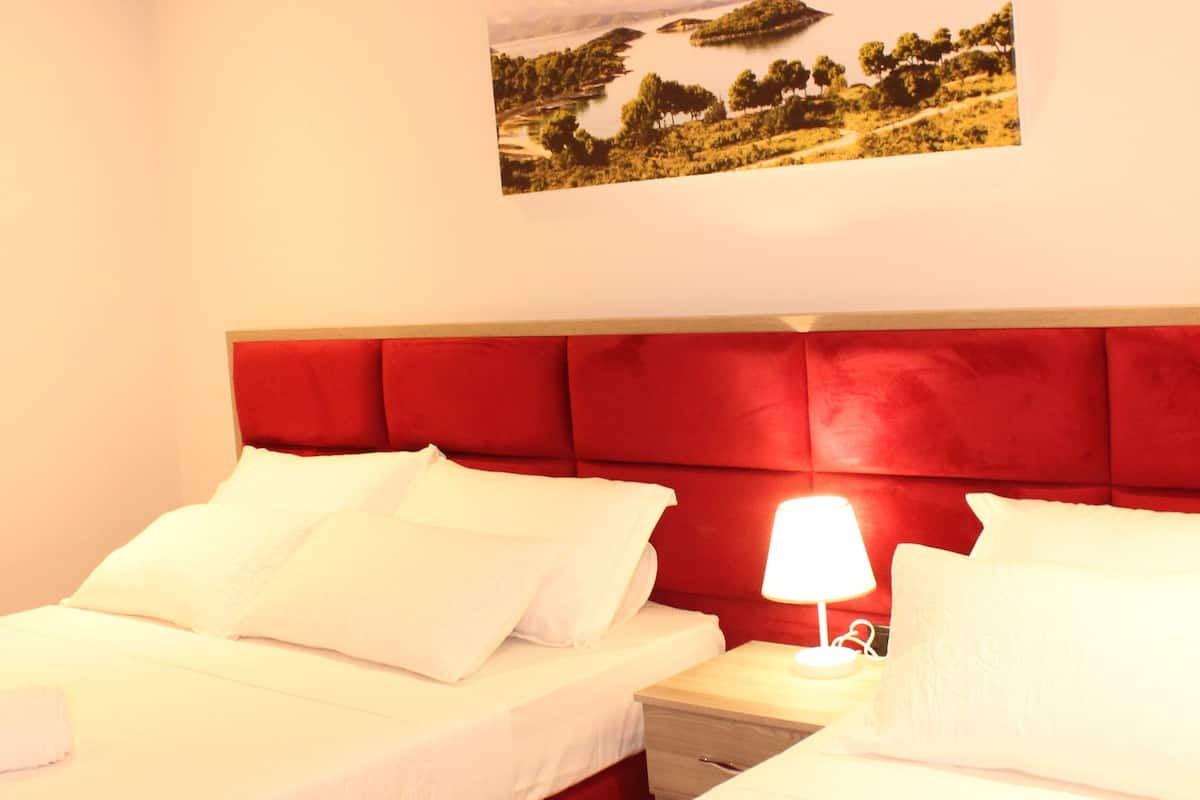 A hotel room with two beds, a red headboard, a nightstand with a lamp, and a painting on the wall.