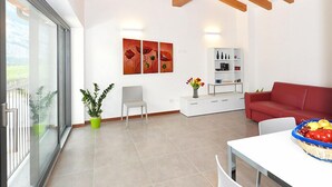 Un saló modern amb un sofà vermell, una taula de menjador blanca i una porta de vidre que dona a un balcó.