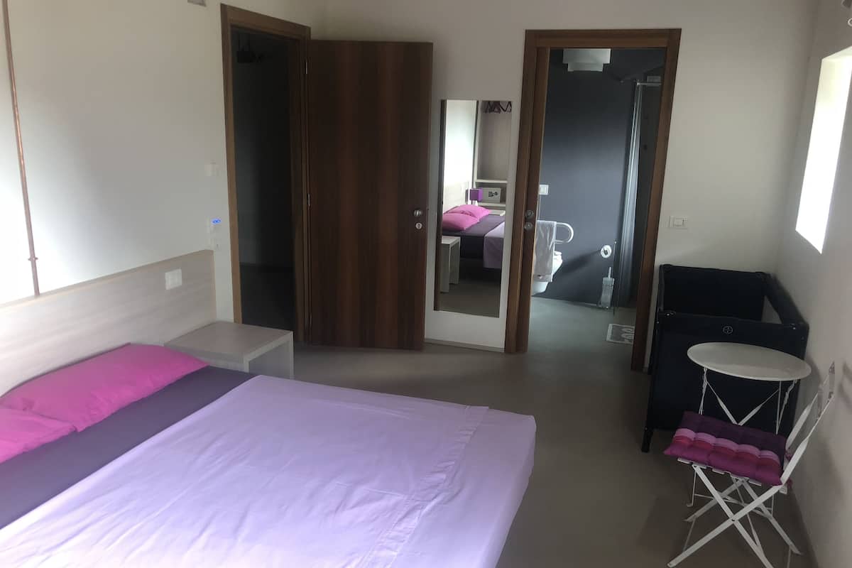 Une chambre à coucher avec un lit, une petite table, une chaise, une armoire et un miroir.
