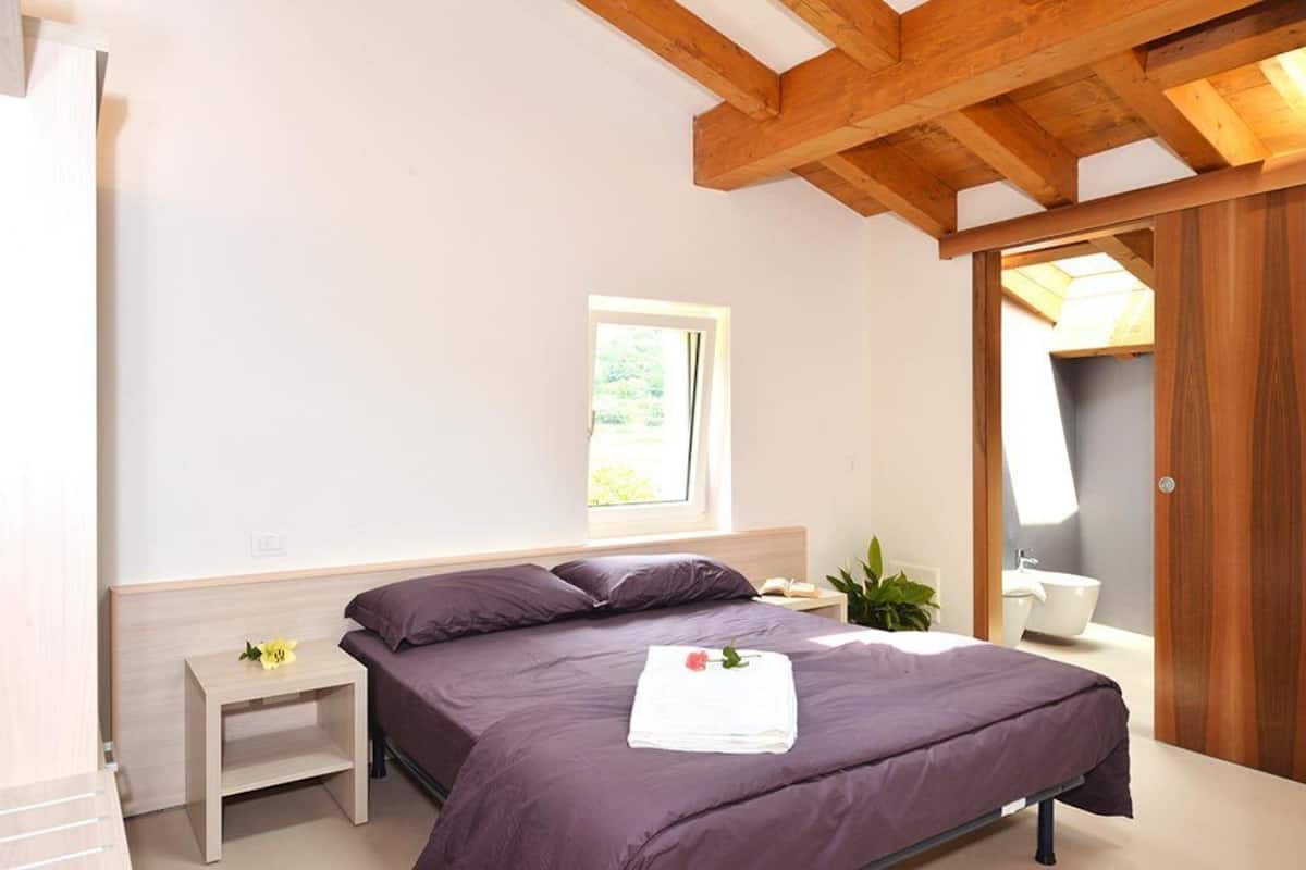 Une chambre à coucher comprenant un lit, une table de chevet, une fenêtre, une plante, et une salle de bain avec une baignoire.