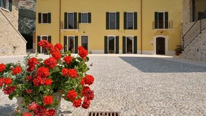 Un edifici groc amb nombroses finestres i balcons, un pati empedrat i flors vermelles al primer pla.