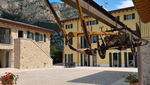 Un pati amb un edifici de pedra, una estructura metàl·lica i un paisatge de muntanya de fons.
