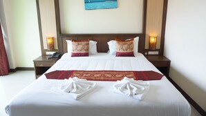 A neatly made hotel room with a large bed, two nightstands, a painting of a beach scene, and a red decorative runner. - Arita House (Patong)