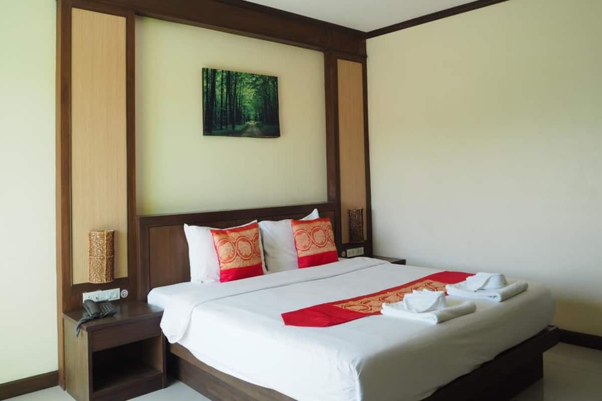 A hotel room with a large bed, a nightstand with a phone, and a painting of a forest on the wall.