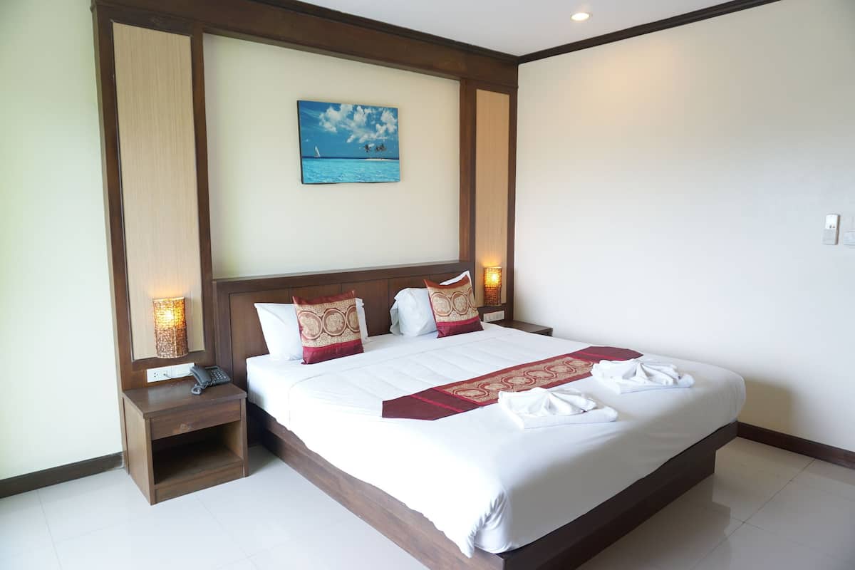 A hotel room with a large bed, a nightstand with a phone, a wall-mounted painting, and a bedside lamp.