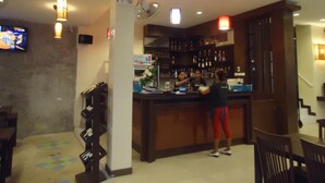 A bar area with a counter, shelves with bottles, and a television on the wall. - Arita House (Patong)