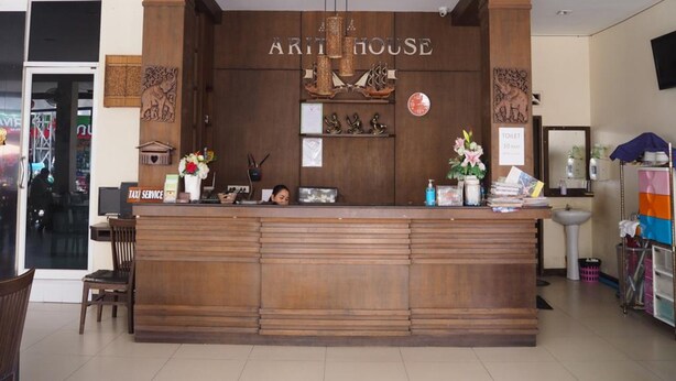 A reception desk with a wooden finish, a sign reading "ARITHOUSE," and a "TOILET 10 M" sign. - Arita House (Patong)