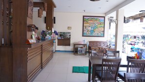 A restaurant with wooden furniture, a counter with a sign, a painting on the wall, and a view of the street outside. - Arita House (Patong)