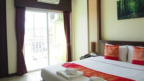 A hotel room with a large bed, red and white bedding, a painting on the wall, and a view through the window. - Arita House (Patong)