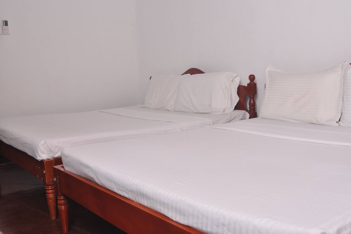 Ein Zimmer mit zwei Einzelbetten, Holz-Kopfteilen, weißen Laken und einer schlichten weißen Wand.