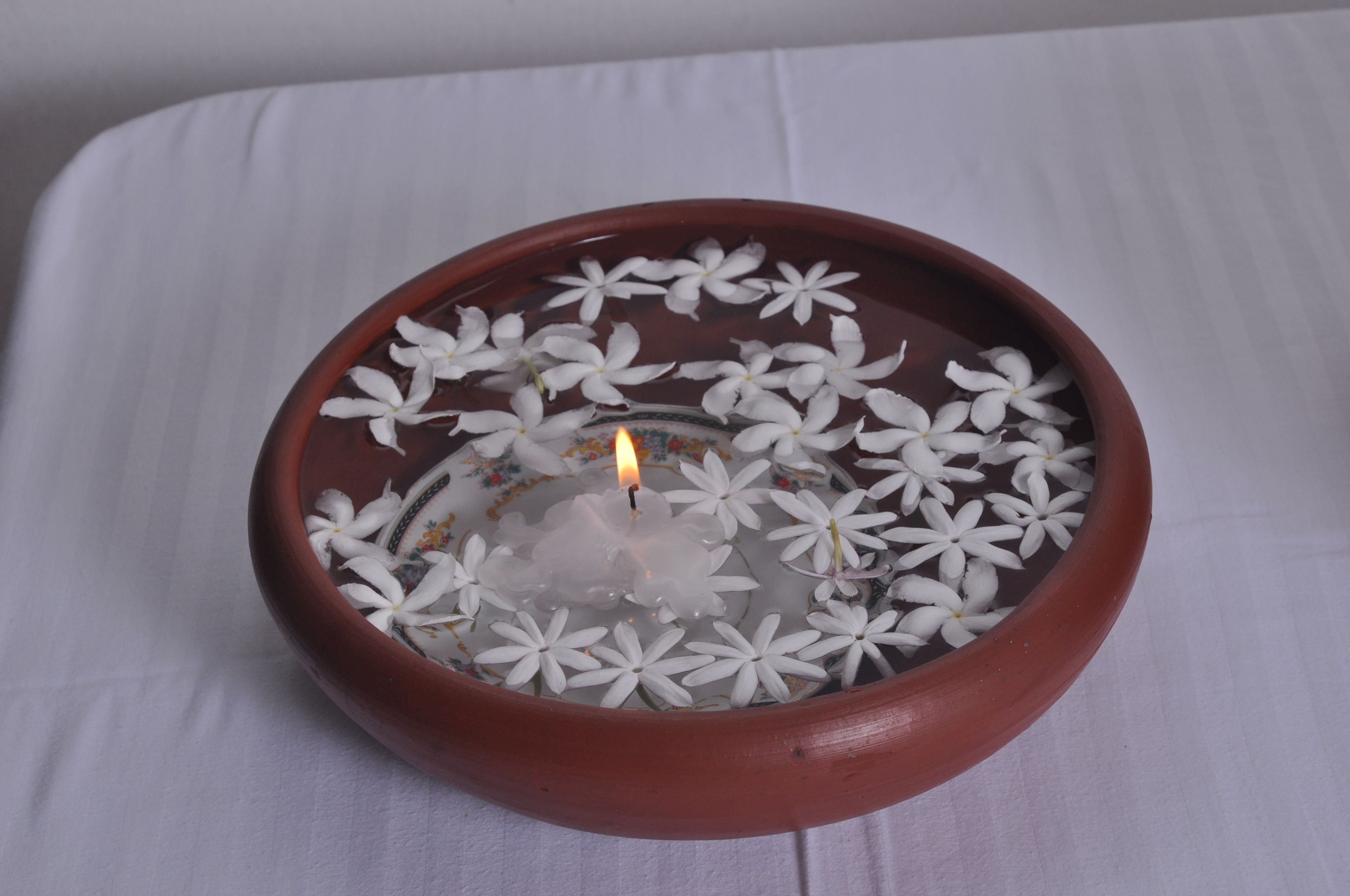 Un bol en terre cuite rempli de fleurs blanches et une bougie allumée.