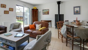 A living room with a brown leather sofa, a wooden coffee table, and a dining area with a table set for four. There is a fireplace and a window with a view of the outdoors. - Beautiful private villa for 8 guests with WIFI, TV, terrace and pets allowed (Port Blanc)