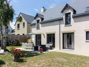 A modern two-story house with a patio area, outdoor seating, and a garden with red flowers. - Stunning private villa for 8 people with WIFI, TV, terrace and pets allowed (Port Blanc)