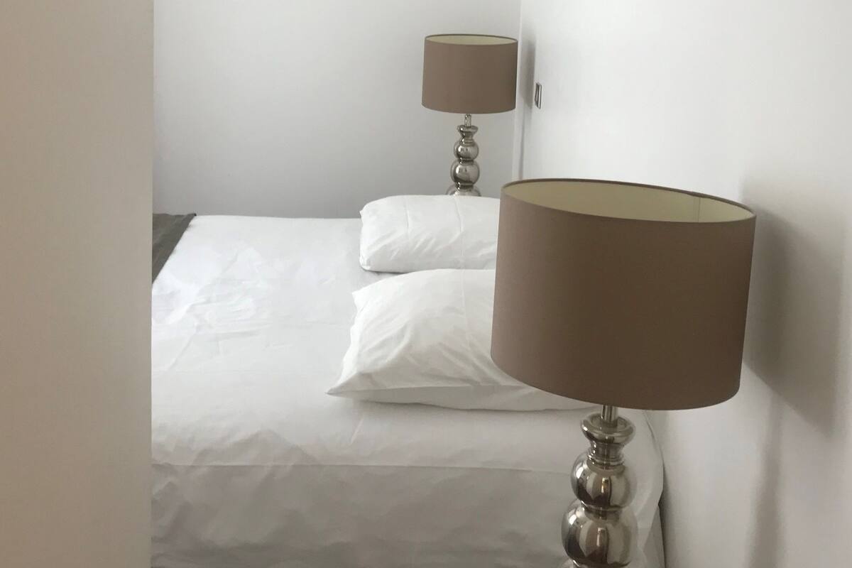 Een hotelkamer met een bed, twee bedlampjes en een effen witte muur.